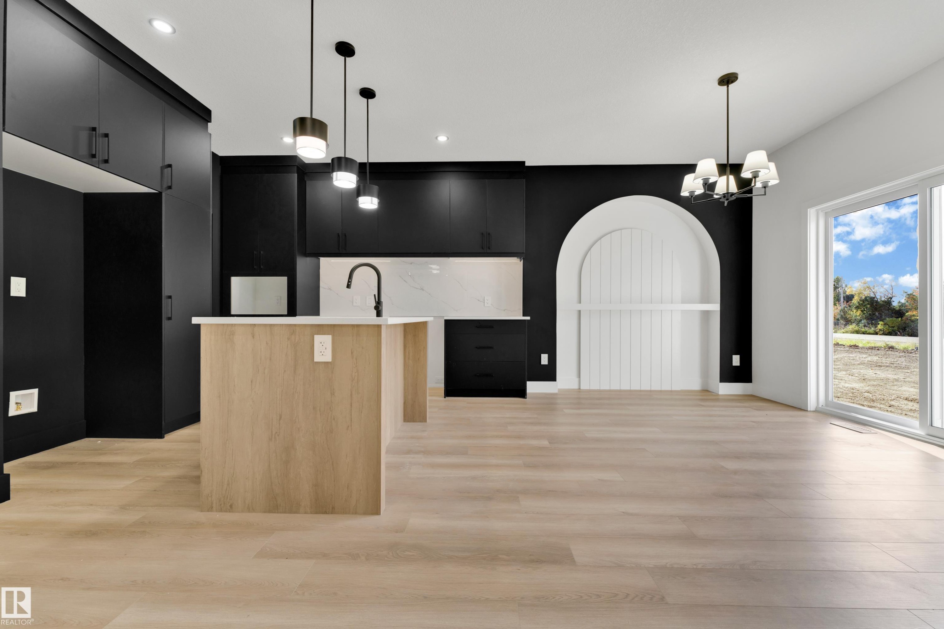 Modern kitchen featuring black cabinetry, light wood-finish flooring, a kitchen island with pendant lighting, white countertops, and a built-in arched feature - 261 Linden Loop, Leduc, AB