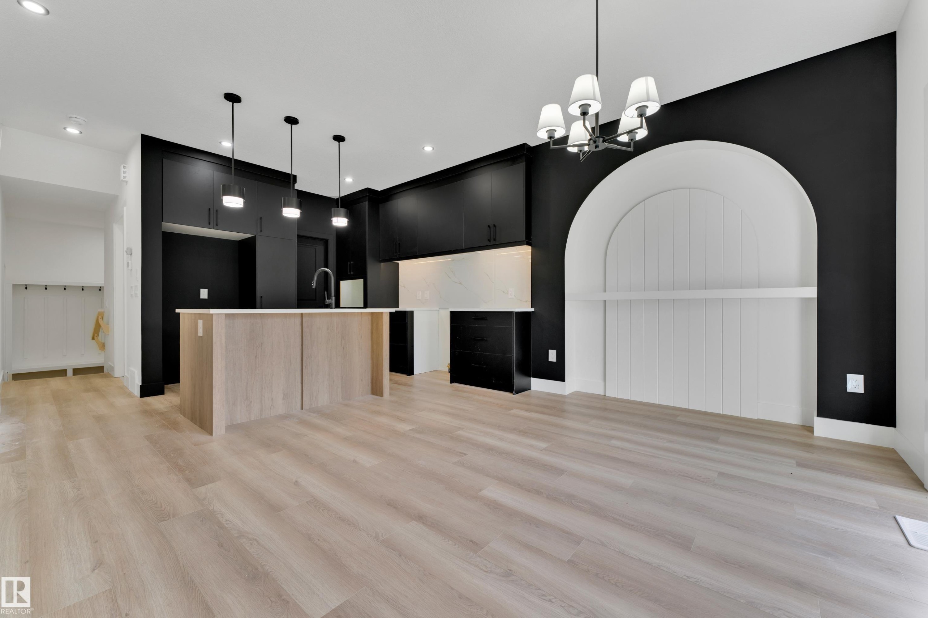 Open-concept living space with light wood-finish flooring, a kitchen island featuring light wood-finish paneling, dark cabinetry, and an arched built-in niche with a shelf - 261 Linden Loop, Leduc, AB