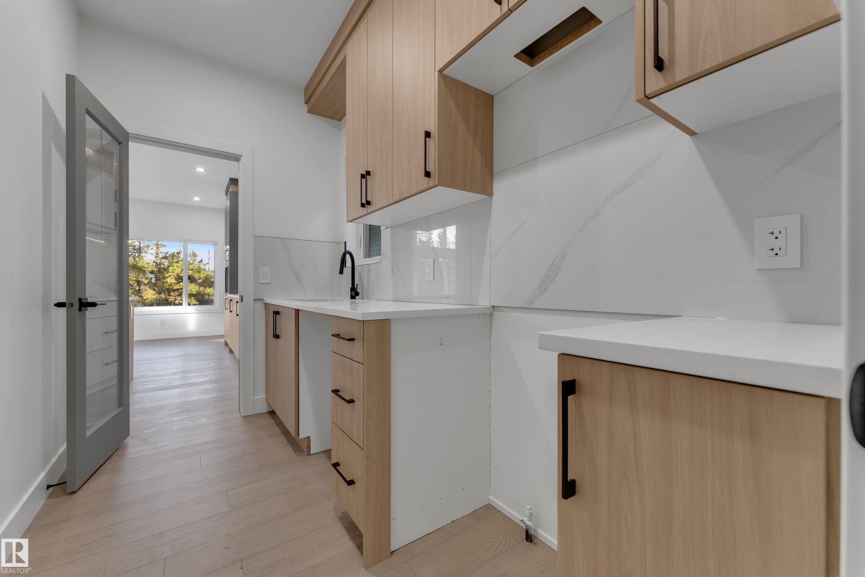 White countertop with an undermount sink, matte black faucet, wood-finish cabinetry, and a white backsplash featuring subtle veining - 247 Linden Loop, Leduc, AB