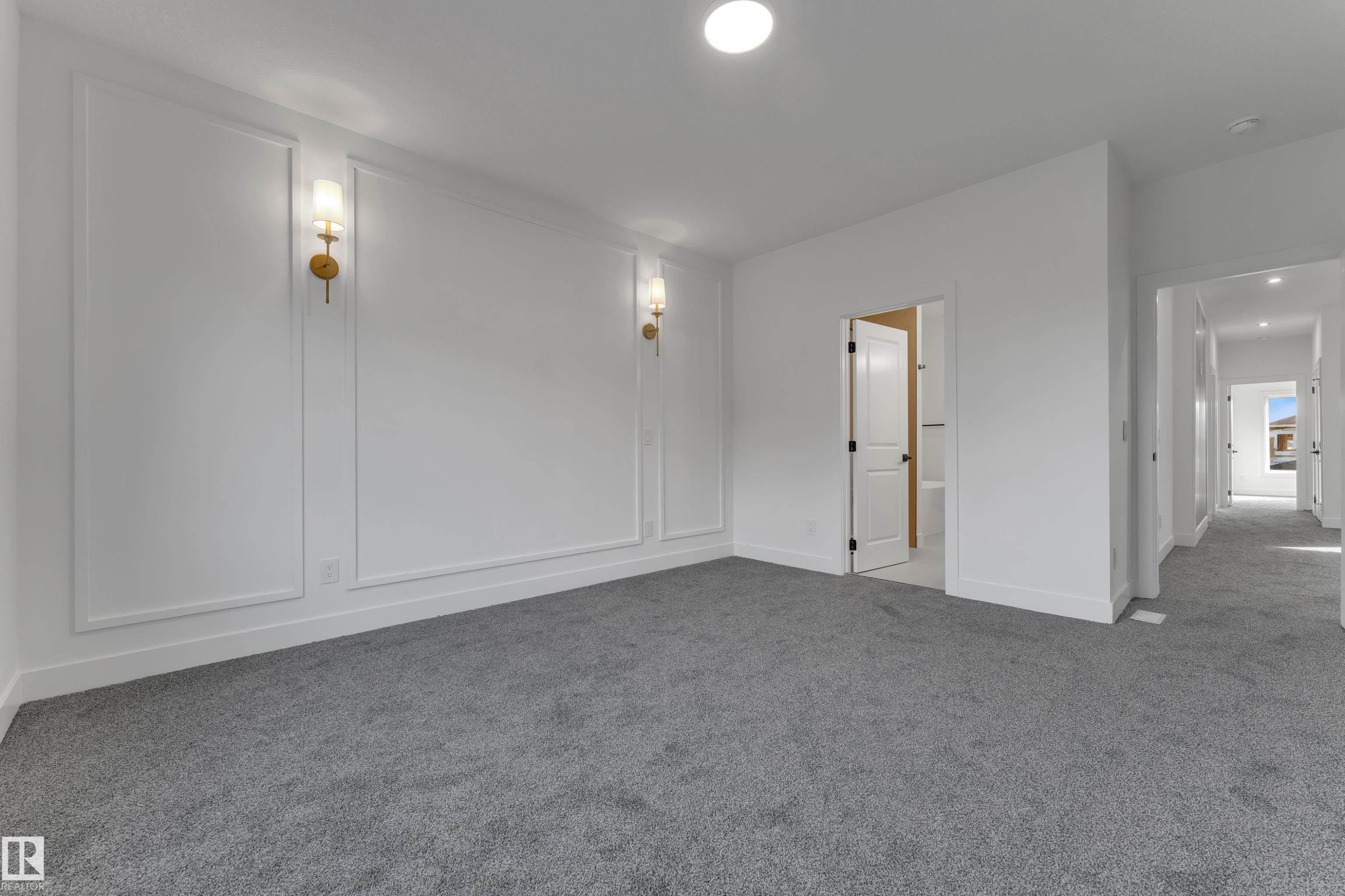 Spacious room featuring accent walls with decorative molding, wall-mounted sconces, recessed lighting, and soft gray carpeting - 247 Linden Loop, Leduc, AB
