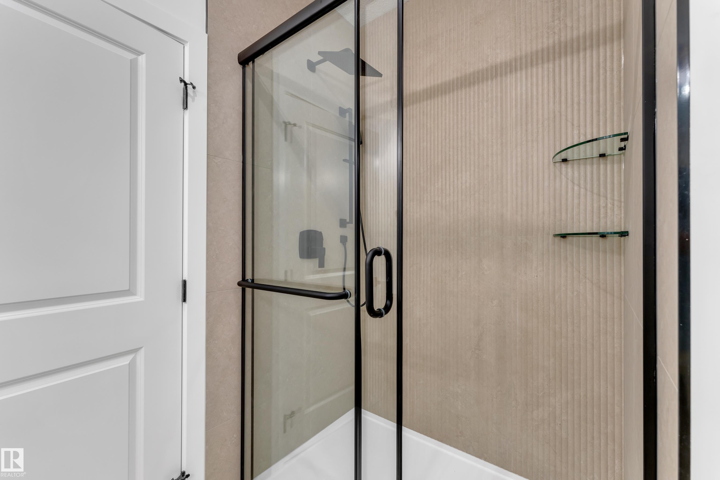 Frameless glass shower enclosure with matte black hardware, textured wall tile, and built-in glass shelves - 247 Linden Loop, Leduc, AB
