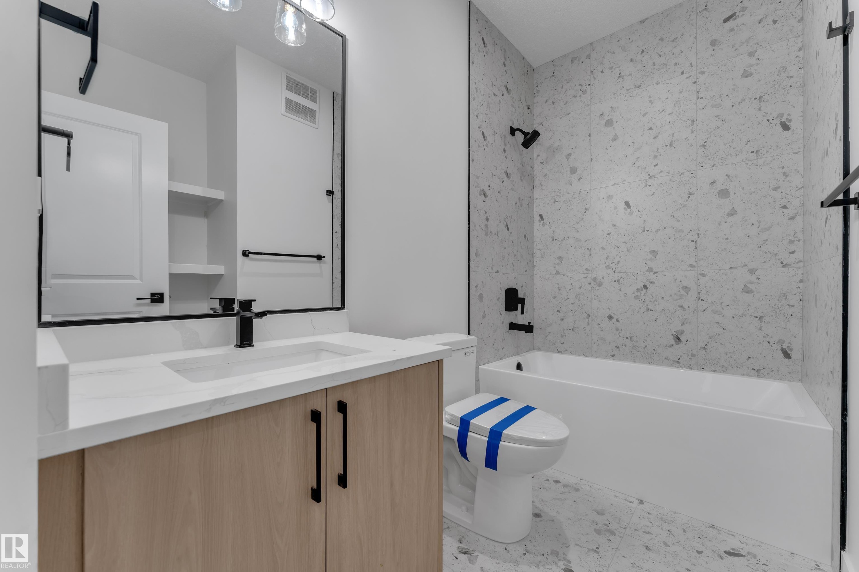 Bathroom vanity with wood-finish cabinetry, integrated sink, and matte black fixtures - 247 Linden Loop, Leduc, AB