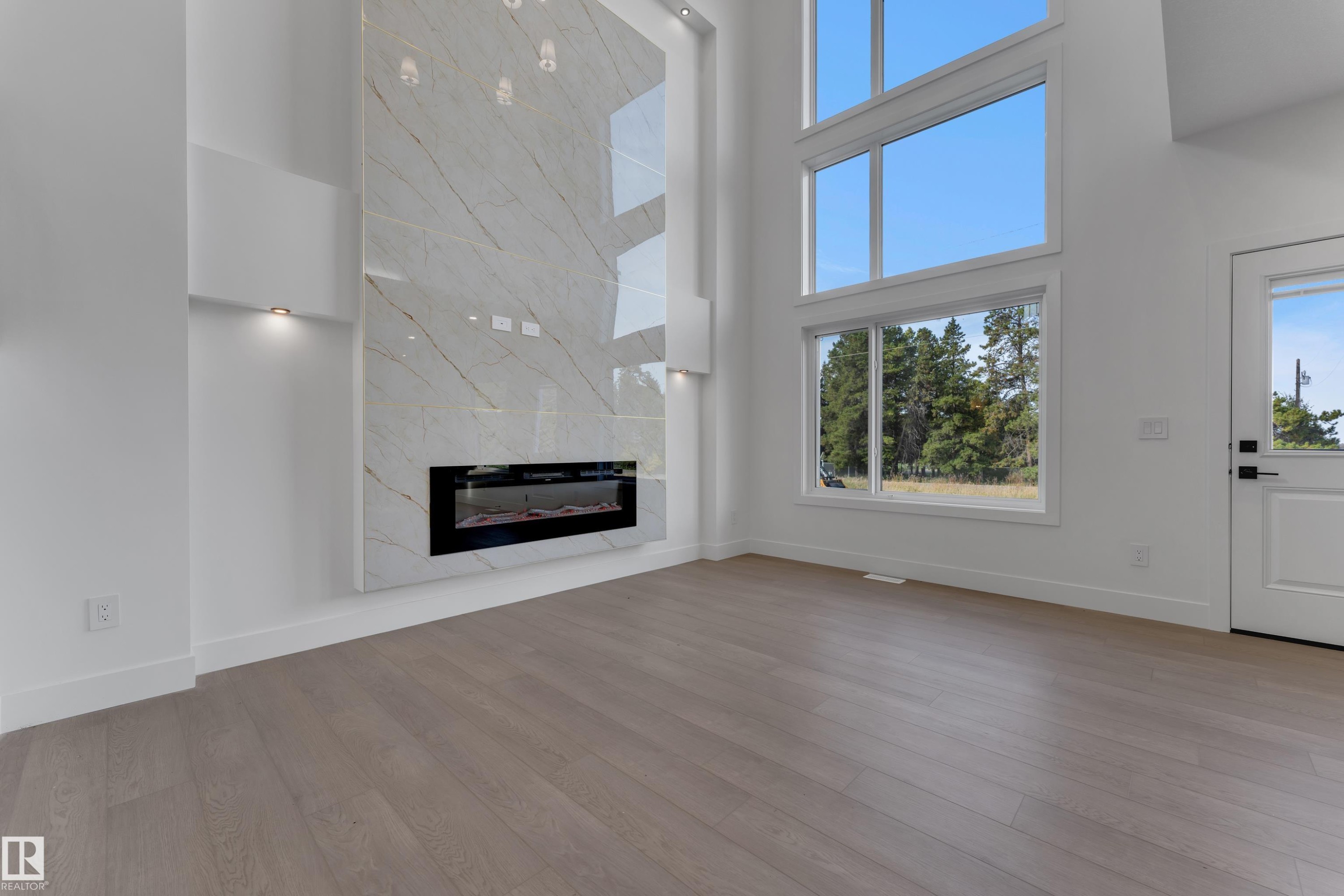 Integrated linear fireplace with a striking floor-to-ceiling tile surround, wood-finish flooring, and expansive windows - 247 Linden Loop, Leduc, AB