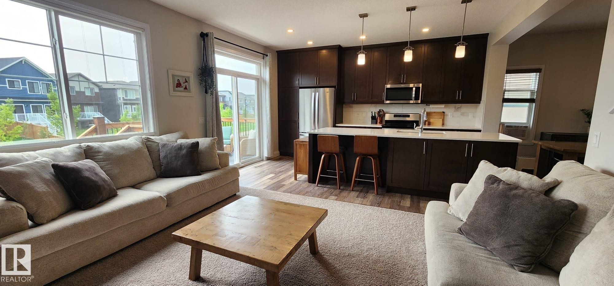 Open-concept living area featuring a kitchen with dark wood-finish cabinetry, stainless steel appliances, and pendant lighting - 3779 Cherry Loop Sw, Edmonton, AB