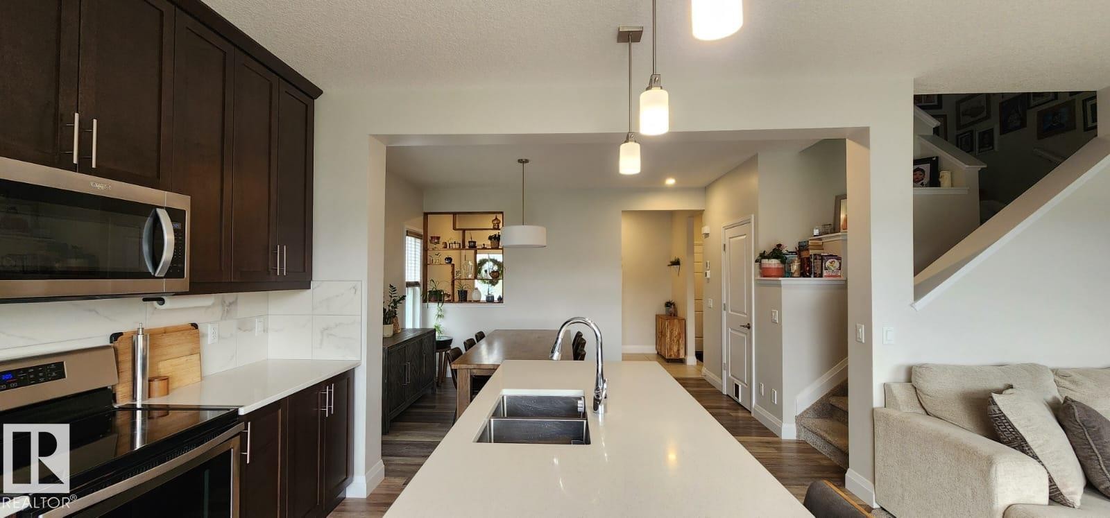 Modern kitchen featuring dark wood-finish cabinetry, stainless steel appliances, and a double basin sink - 3779 Cherry Loop Sw, Edmonton, AB