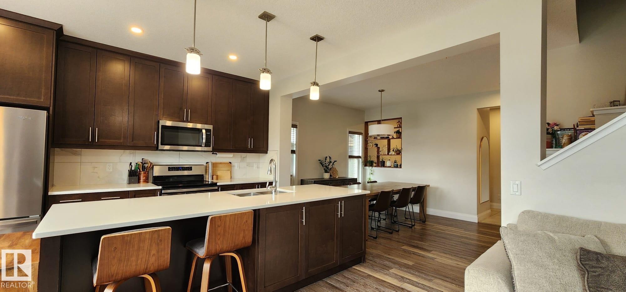 Gourmet kitchen featuring dark wood cabinetry, stainless steel appliances, a center island with seating, pendant lighting, and wood-finish flooring - 3779 Cherry Loop Sw, Edmonton, AB