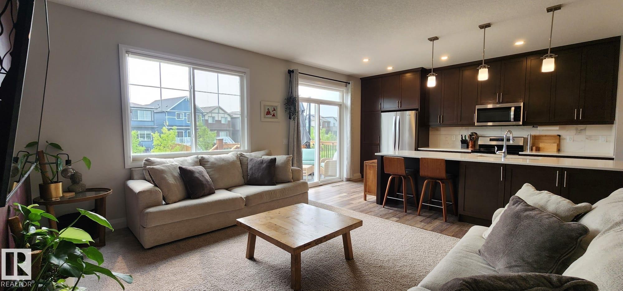 Open-concept living area featuring a kitchen with dark wood-finish cabinetry, stainless steel appliances, and pendant lighting - 3779 Cherry Loop Sw, Edmonton, AB