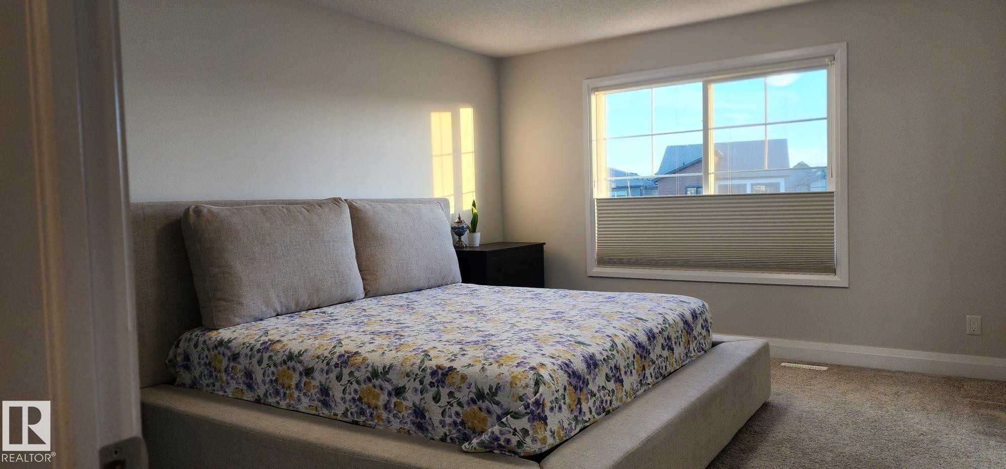 Carpeted room featuring a large window with horizontal blinds, light-toned walls, and a built-in recessed light fixture - 3779 Cherry Loop Sw, Edmonton, AB