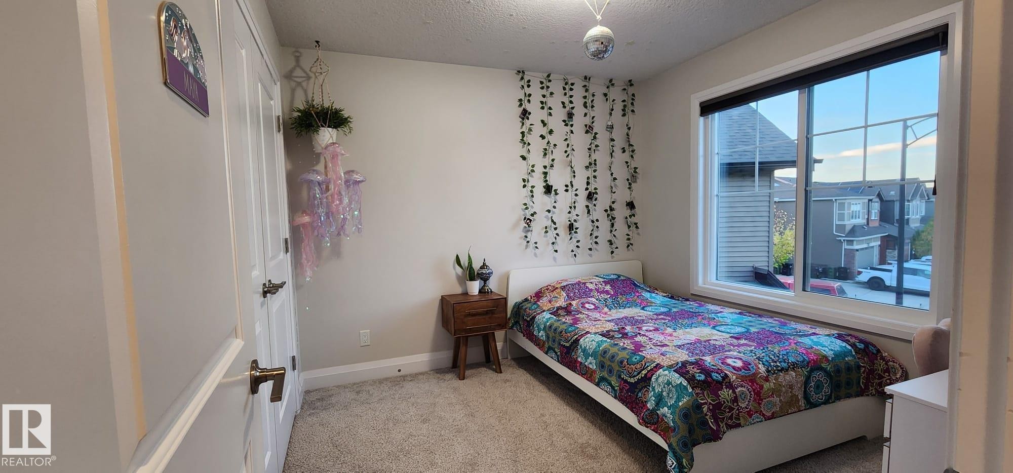 White painted walls with white trim, gray carpet flooring, white door with brushed nickel hardware, and a large window with white framing - 3779 Cherry Loop Sw, Edmonton, AB