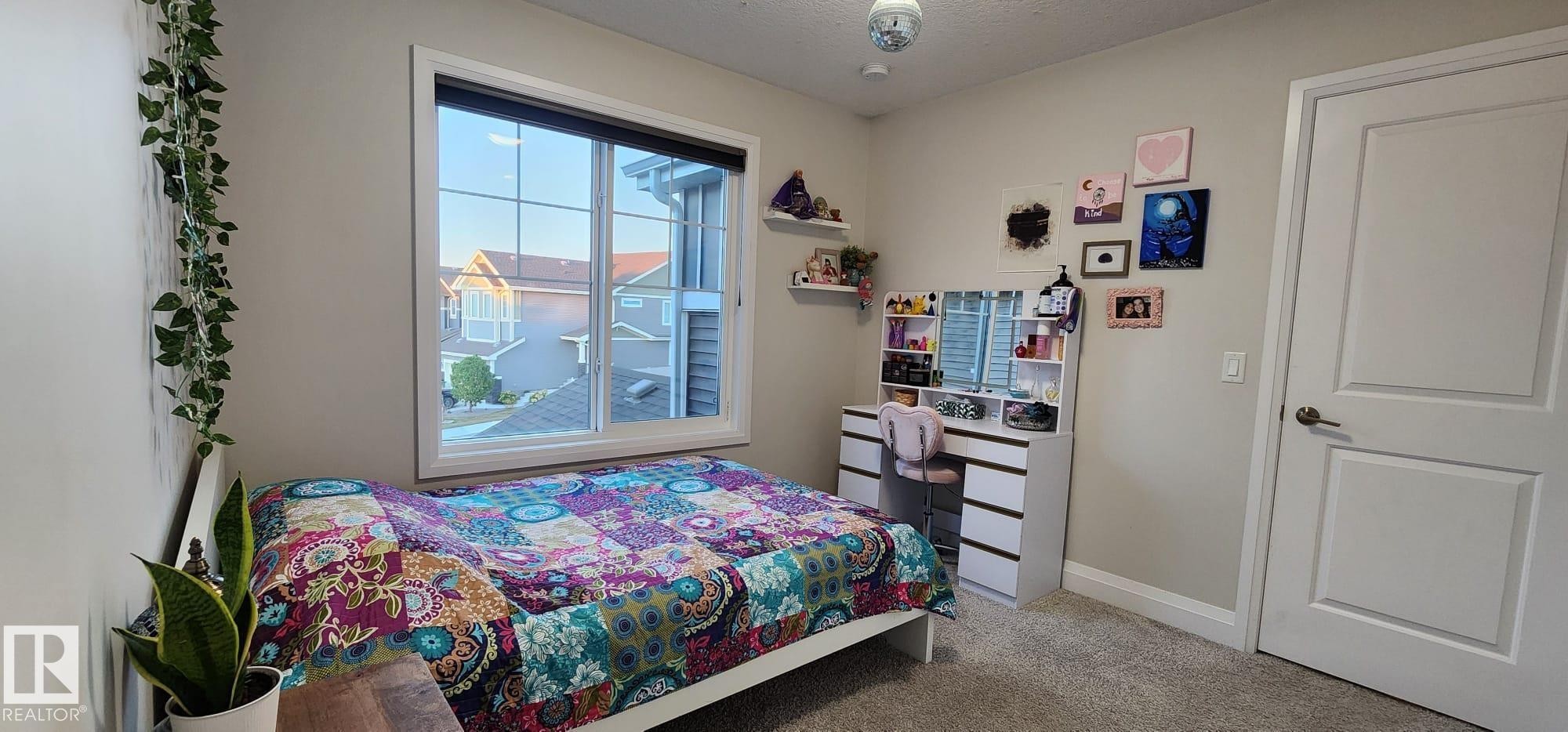 Window with white frame, light gray walls, built-in vanity with drawers, white interior door with paneling, and gray carpeted flooring - 3779 Cherry Loop Sw, Edmonton, AB