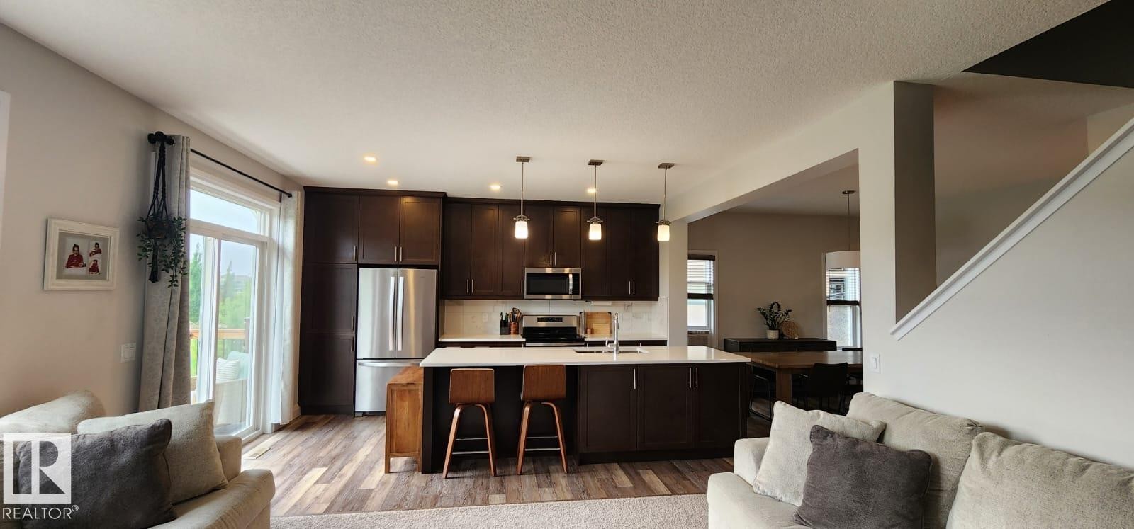 Kitchen featuring dark wood cabinetry, stainless steel appliances, a center island with pendant lighting, and wood-finish flooring - 3779 Cherry Loop Sw, Edmonton, AB