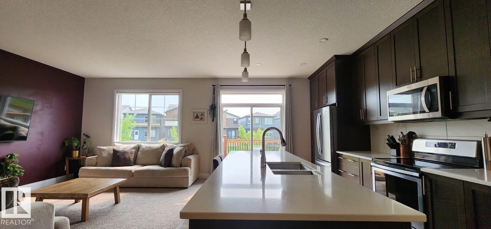 Open-concept living space with a kitchen island featuring an integrated sink and pendant lighting - 3779 Cherry Loop Sw, Edmonton, AB