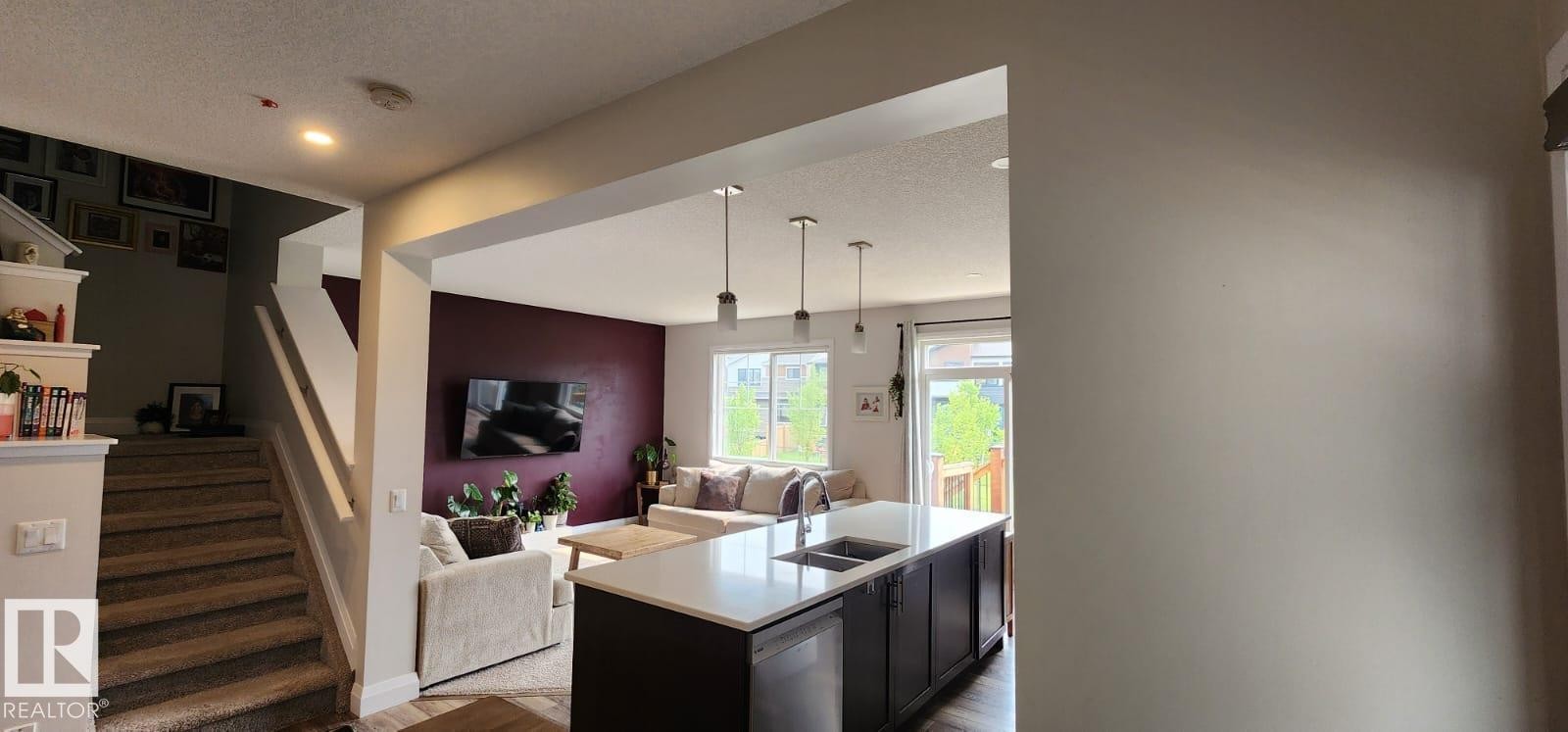 Open-concept living space featuring a kitchen island with sink, pendant lighting, and wood-finish flooring - 3779 Cherry Loop Sw, Edmonton, AB
