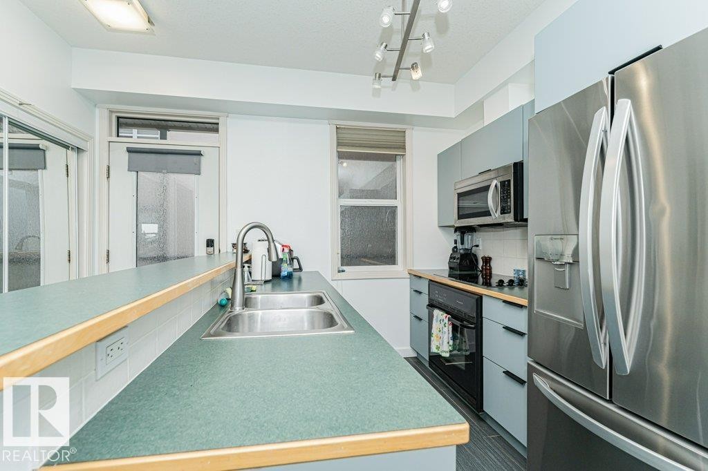 Kitchen with green countertops, stainless steel double-basin sink, stainless steel refrigerator, stainless steel microwave, and track lighting - #202 9503 101 Av Nw, Edmonton, AB