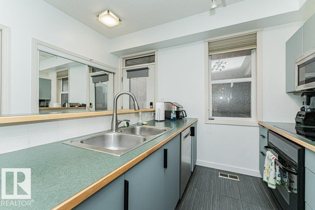 Kitchen featuring a double basin stainless steel sink with a high-arch faucet, gray cabinetry, built-in stainless steel appliances, and dark-toned floor tiling - #202 9503 101 Av Nw, Edmonton, AB