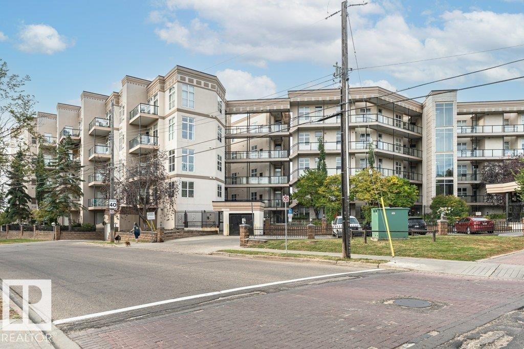 Multi-story building featuring balconies with glass railings, an integrated entrance with an arched portico, and a prominent glass and metal elevator shaft - #202 9503 101 Av Nw, Edmonton, AB