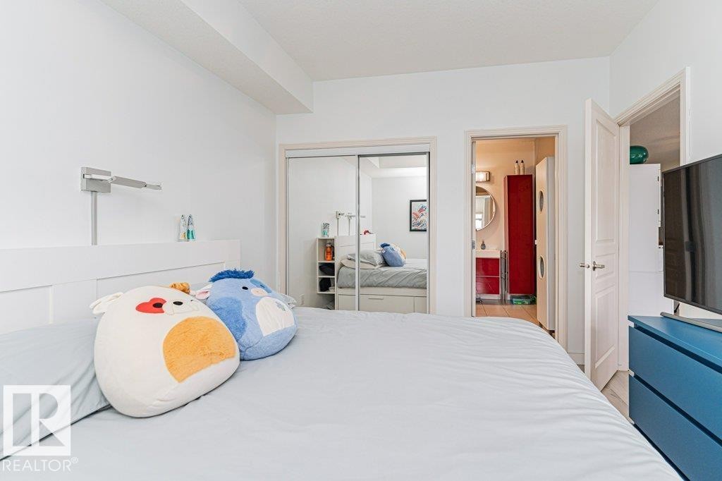 Integrated bedroom with white walls, a built-in wall light, and a mirrored sliding closet door - #202 9503 101 Av Nw, Edmonton, AB
