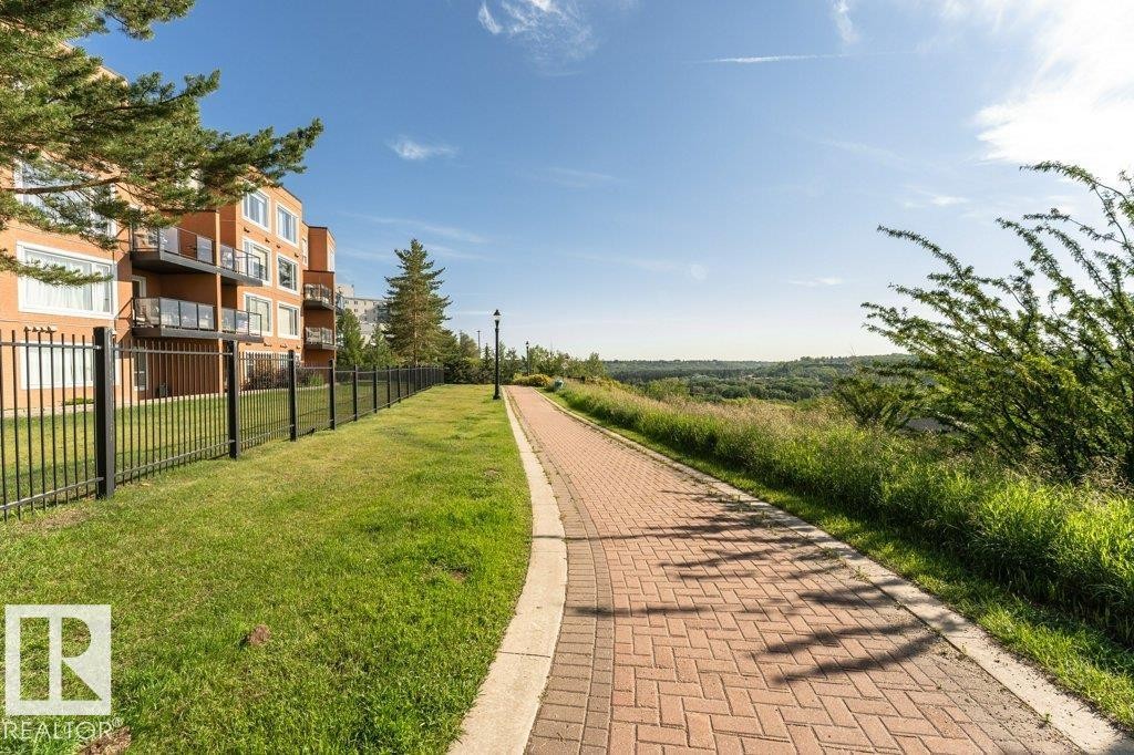 Paved brick pathway with a concrete border, featuring surrounding grassy areas and a distant landscape - #202 9503 101 Av Nw, Edmonton, AB
