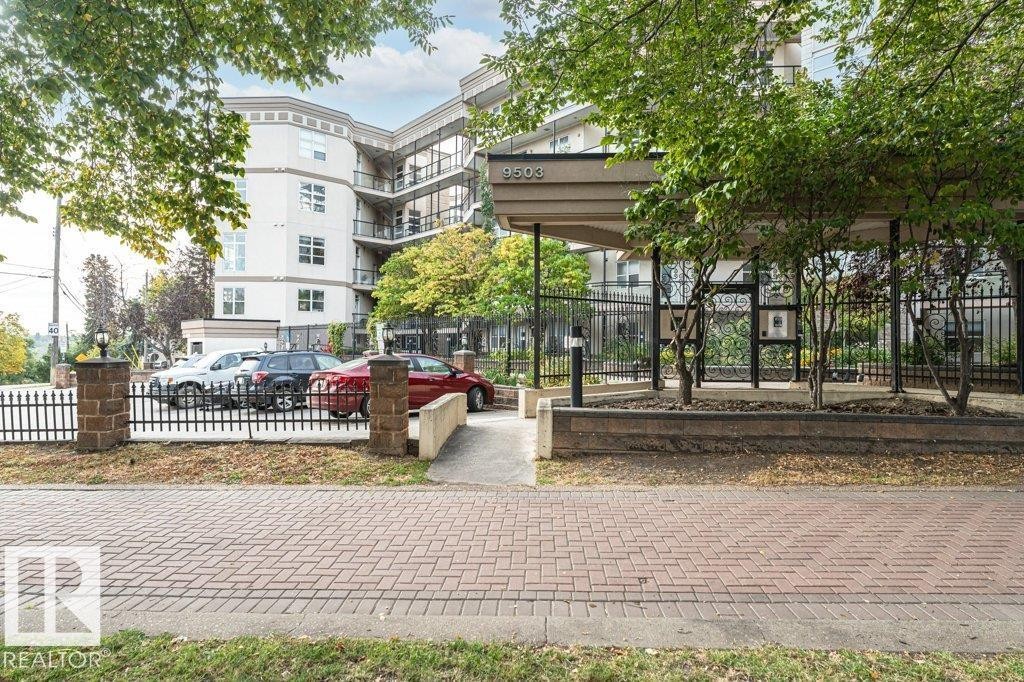 Contemporary building with multiple levels of balconies, a prominent covered entry, and a secure perimeter fence with stone pillars - #202 9503 101 Av Nw, Edmonton, AB