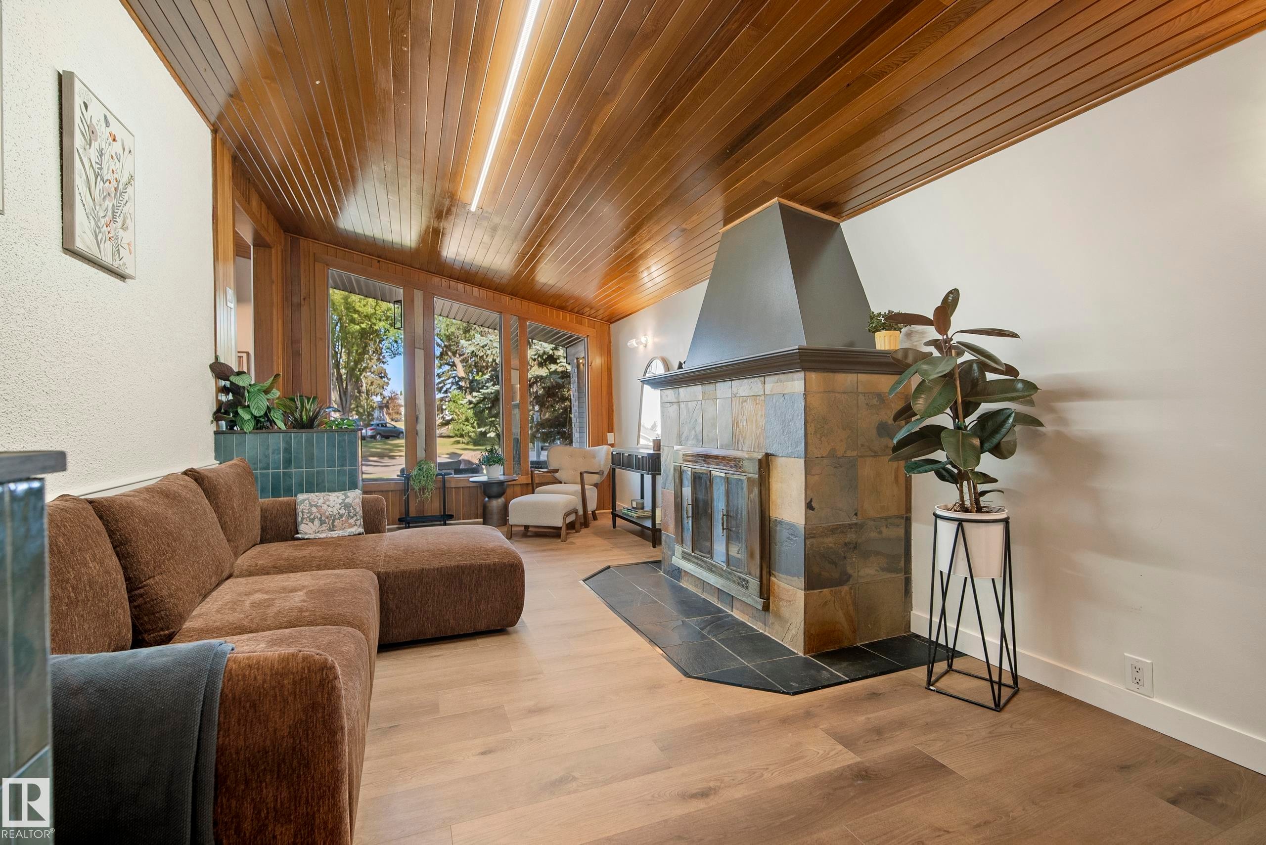 Wood-finish flooring, wood-paneled ceiling, stone-clad fireplace with black metal hood, white wall finishes, and large picture windows - 10316 42 Street Nw, Edmonton, AB