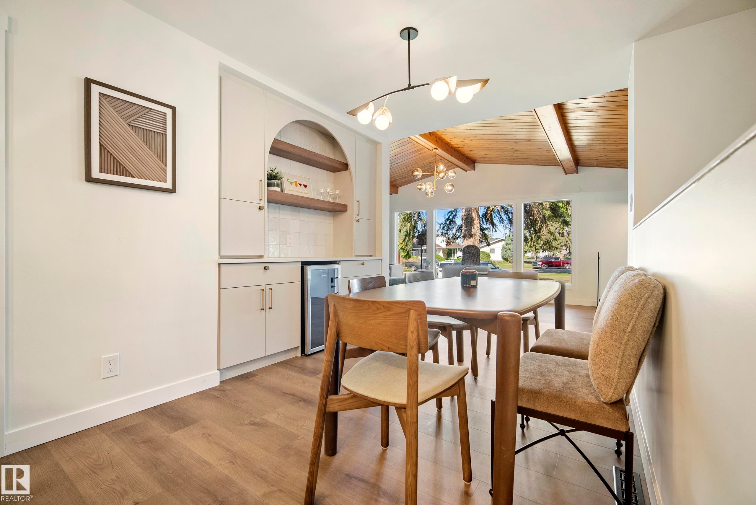 Wood-finish flooring throughout, built-in cabinetry with an arched display niche, recessed beverage refrigerator, contemporary lighting fixtures, and large picture windows - 10316 42 Street Nw, Edmonton, AB