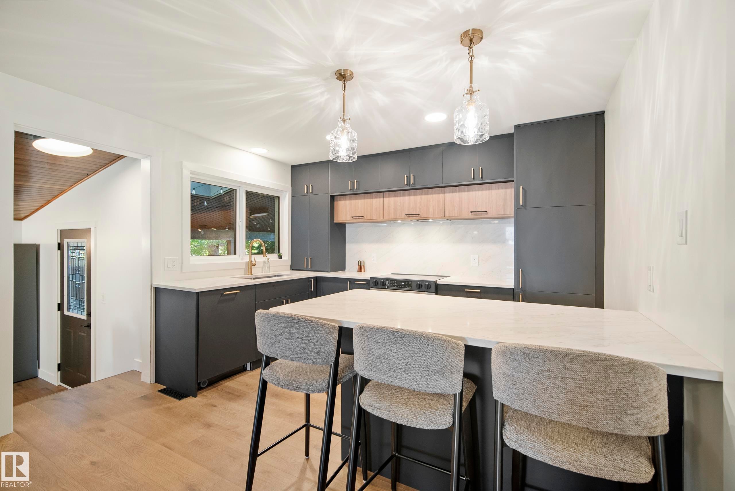Modern kitchen featuring two-tone cabinetry, a central island with countertop seating, wood-finish flooring, and pendant lighting fixtures - 10316 42 Street Nw, Edmonton, AB