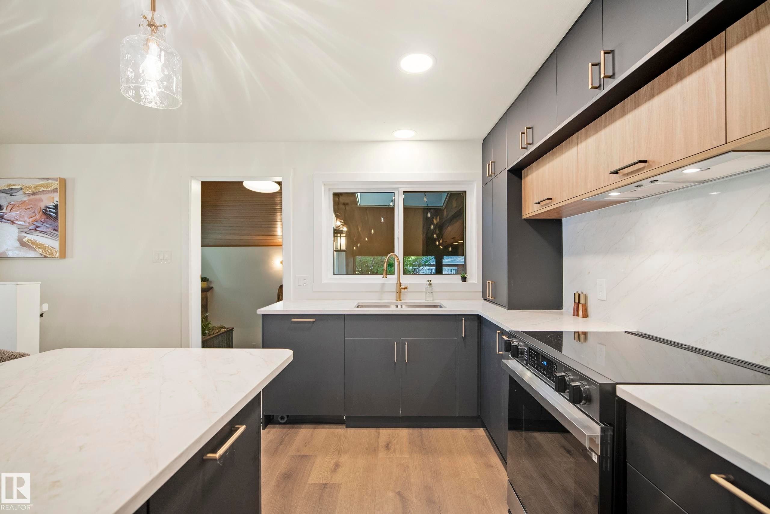 Modern kitchen featuring two-tone cabinetry, light-toned countertops, a built-in range, wood-finish flooring, and a single basin sink with a gold-tone faucet - 10316 42 Street Nw, Edmonton, AB