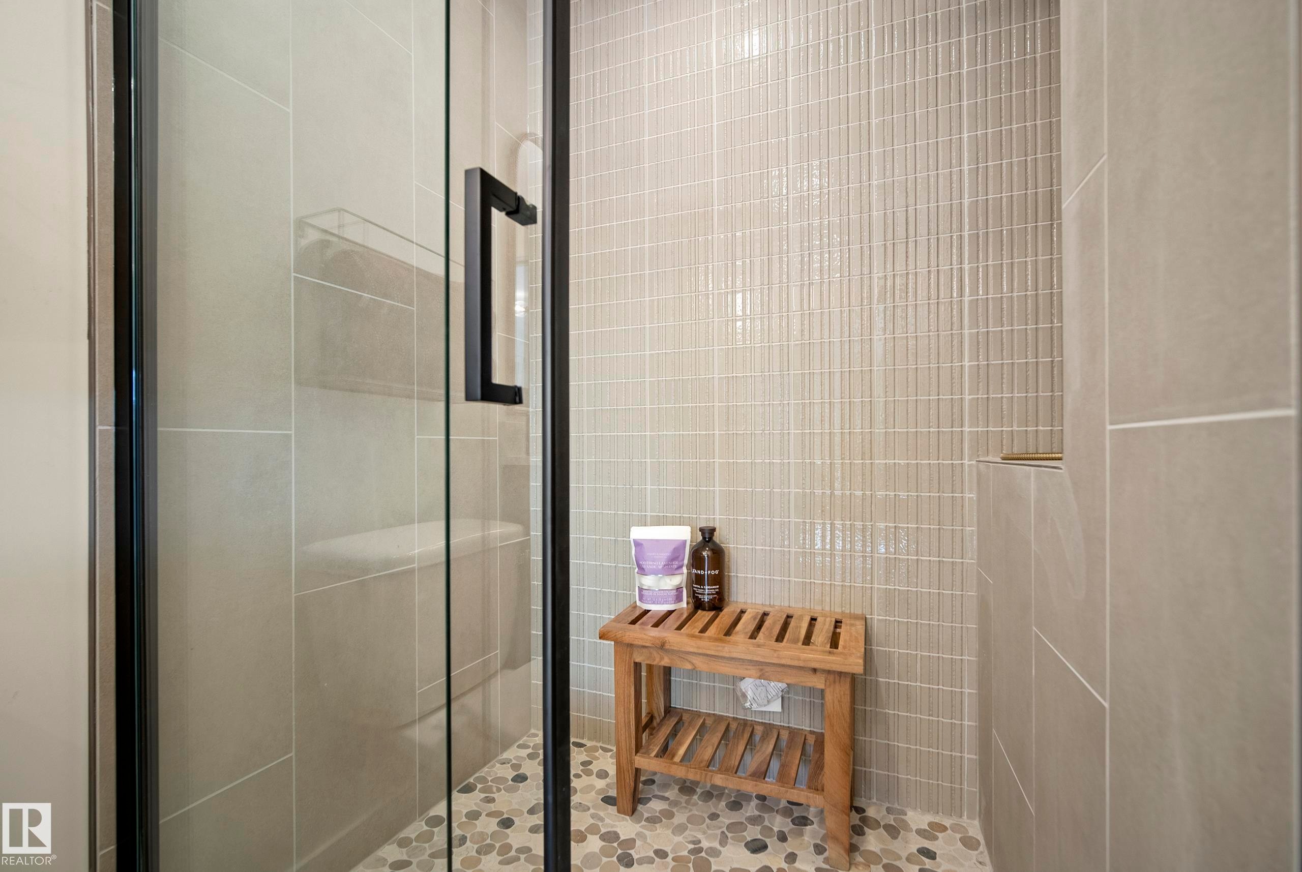 Frameless glass shower enclosure with matte black hardware, pebble-tiled shower floor, and vertical subway tile accent wall - 10316 42 Street Nw, Edmonton, AB