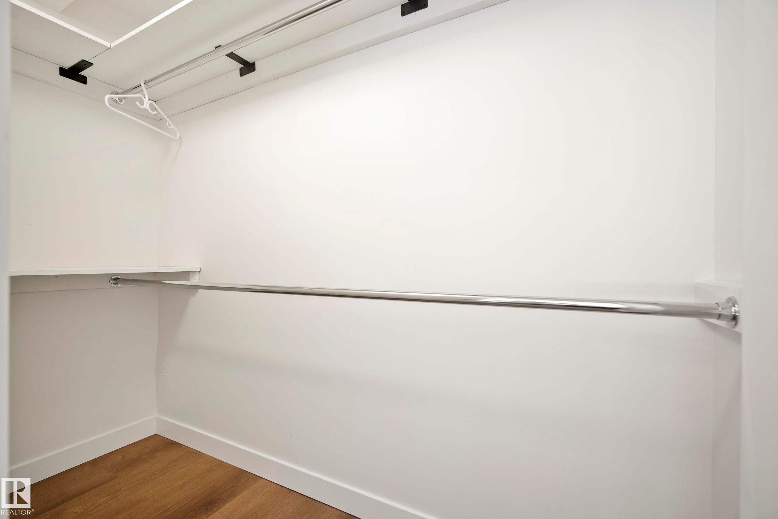 Built-in closet with wood-finish flooring, white walls, and chrome hanging rods - 10316 42 Street Nw, Edmonton, AB