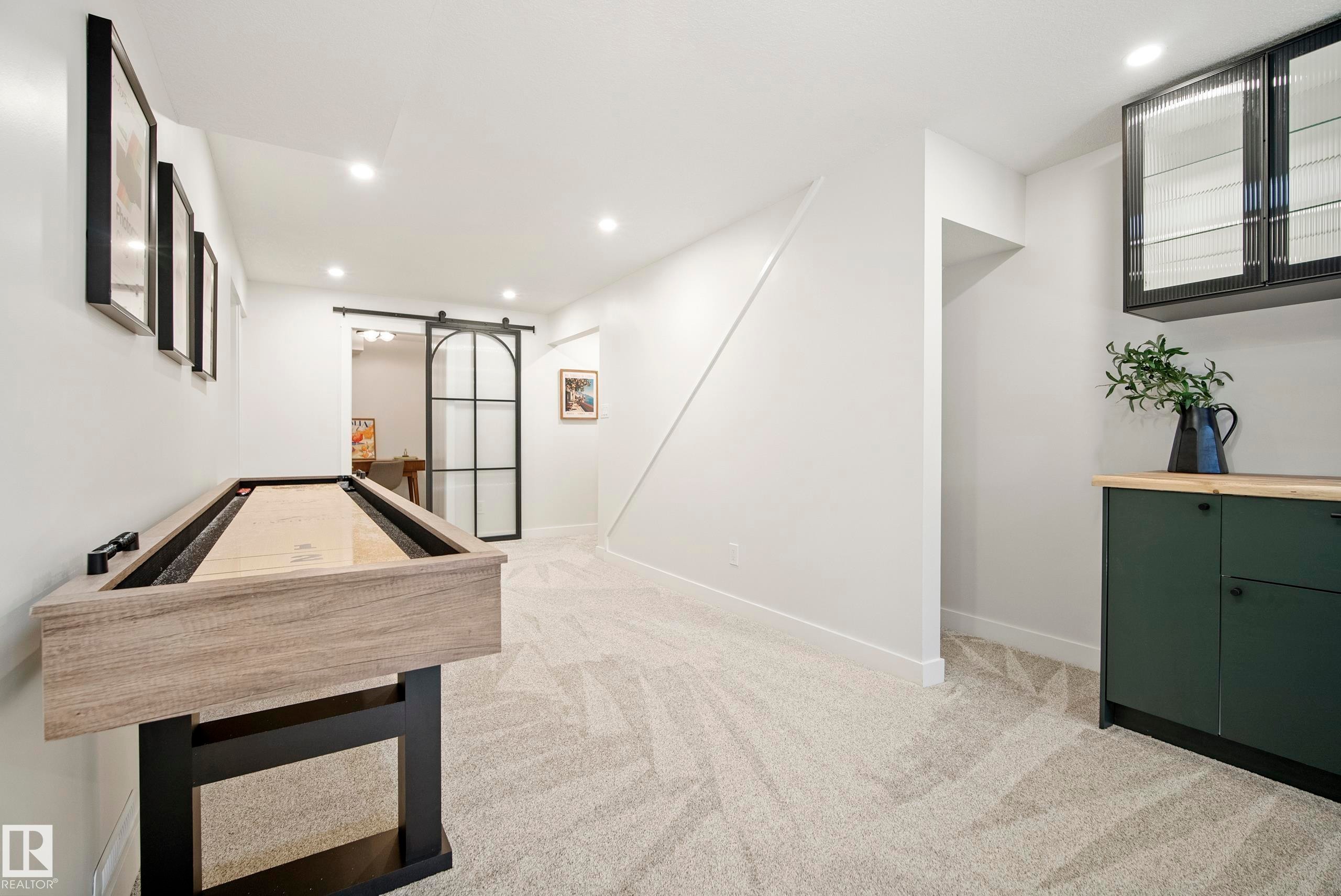 Recessed lighting, light-toned carpeting, built-in cabinetry with a wood-finish countertop, dark-toned upper cabinetry with fluted glass, and a black framed sliding barn door - 10316 42 Street Nw, Edmonton, AB