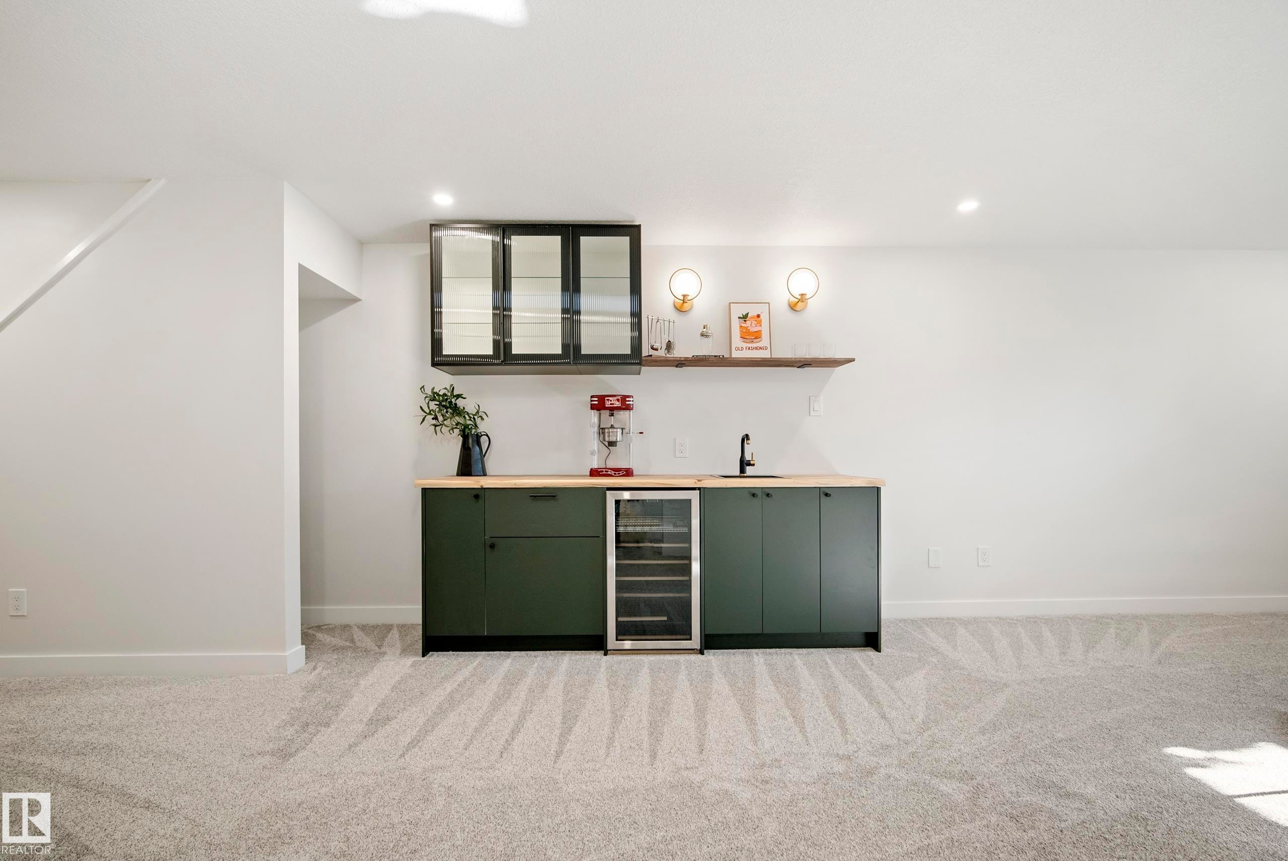 Built-in wet bar with wood-finish countertop, under-counter beverage refrigerator, dark green cabinetry, and a floating wood shelf - 10316 42 Street Nw, Edmonton, AB