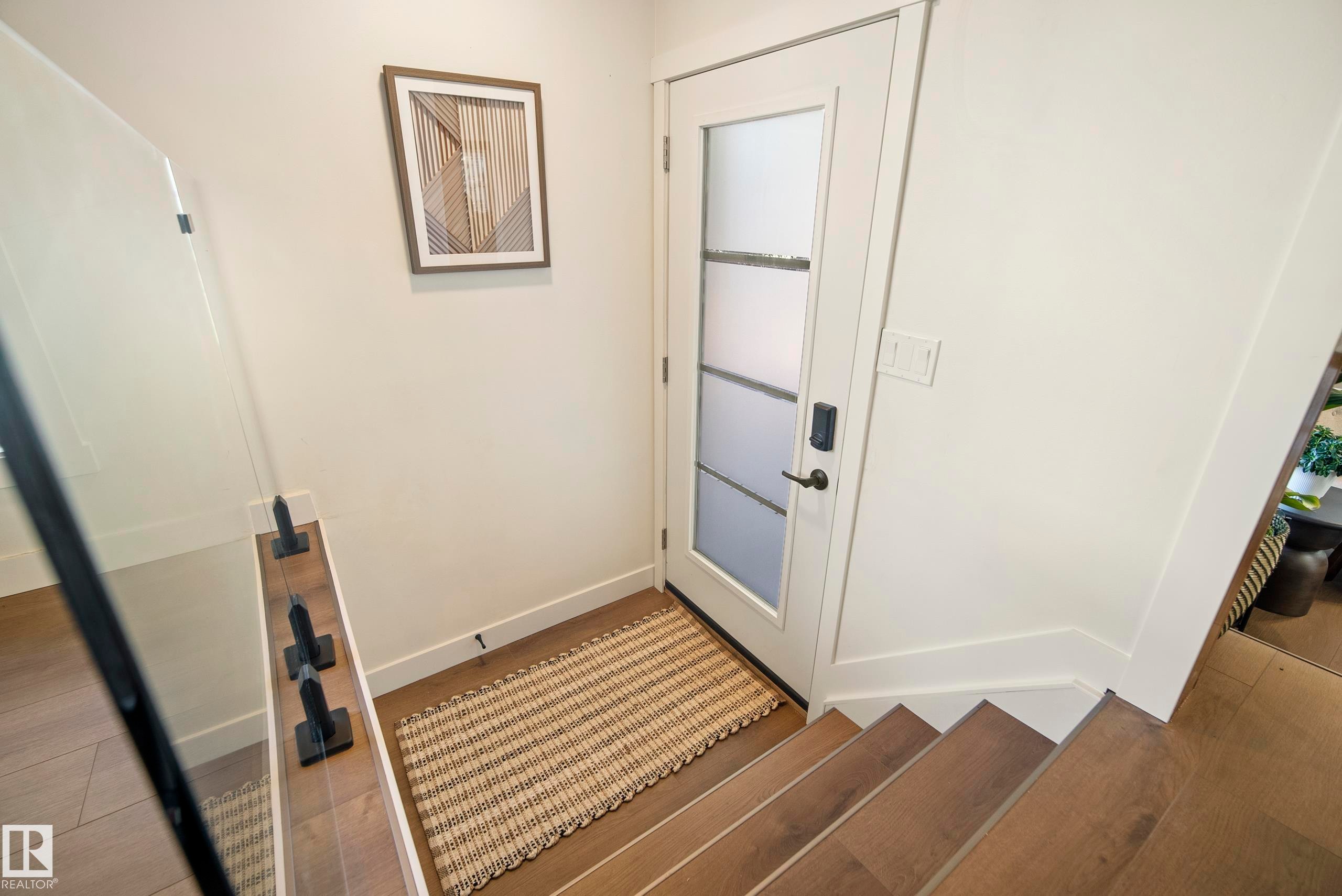 Entryway featuring a white door with frosted glass panels, matte black door hardware, and wood-finish flooring extending to the staircase - 10316 42 Street Nw, Edmonton, AB