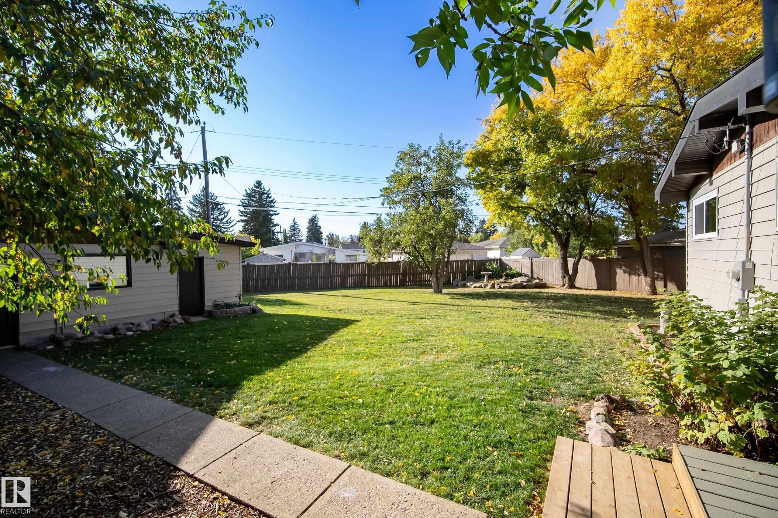 Expansive backyard featuring a manicured lawn, mature trees, and a privacy fence - 10316 42 Street Nw, Edmonton, AB