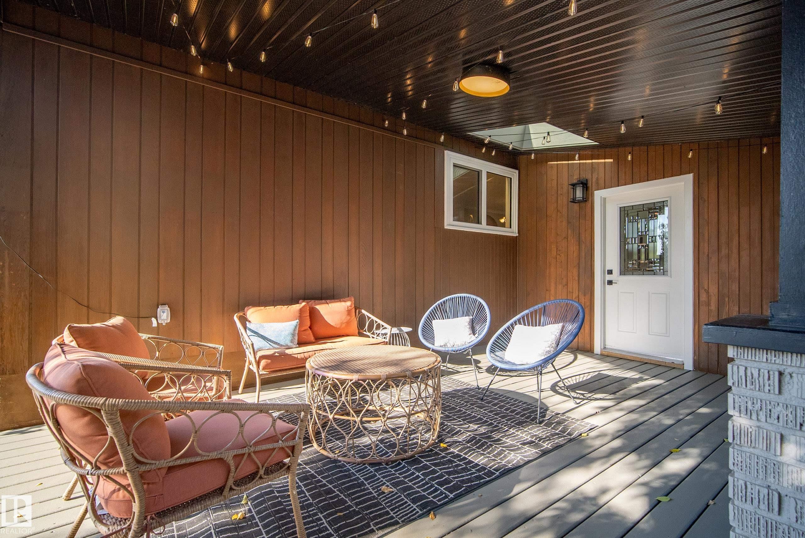 Covered deck with a wood-finish ceiling, vertical wood-panel siding, and a white entry door with decorative glass - 10316 42 Street Nw, Edmonton, AB