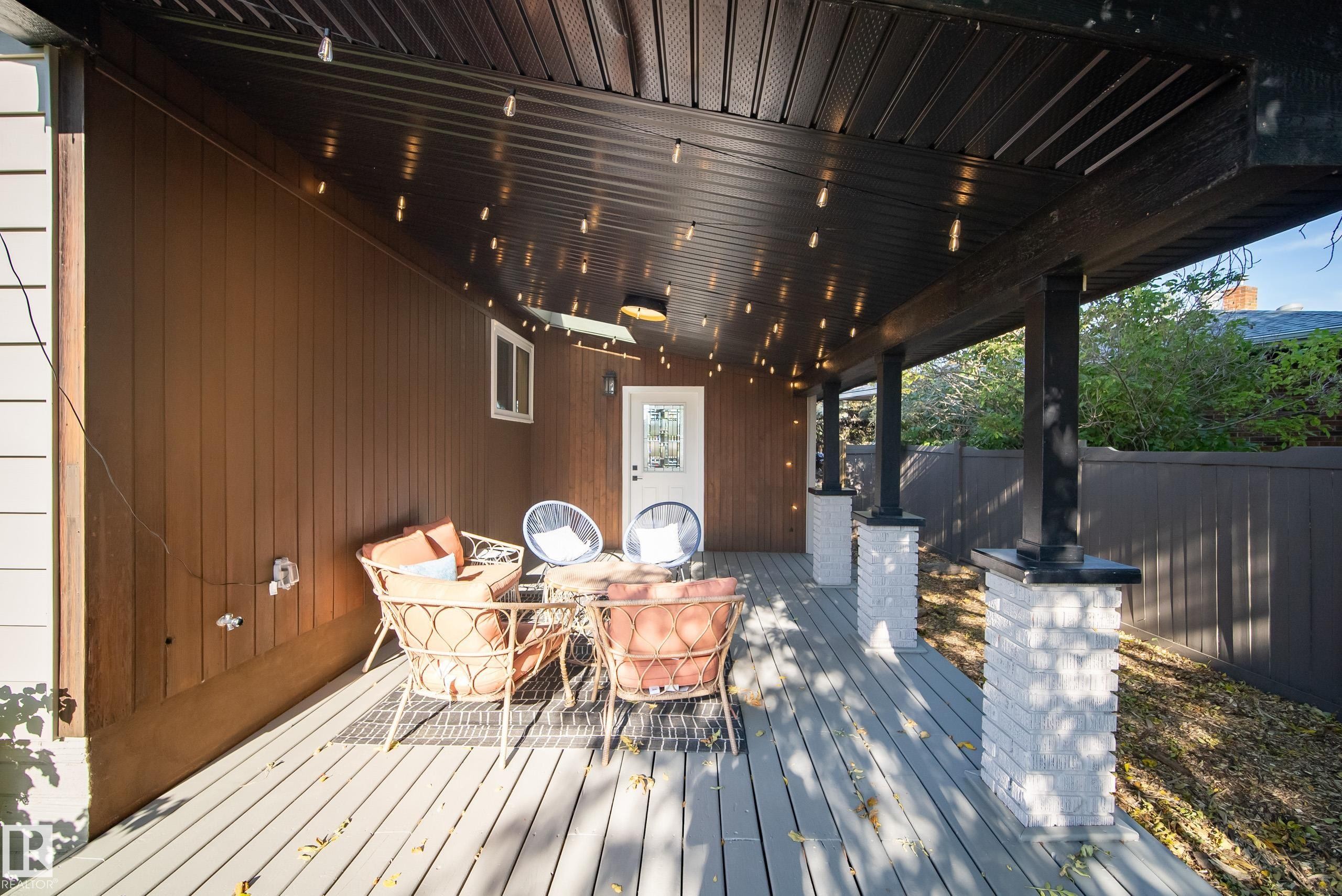 Covered patio featuring a wood-finish deck, vertical wood siding, and white brick-clad support columns - 10316 42 Street Nw, Edmonton, AB