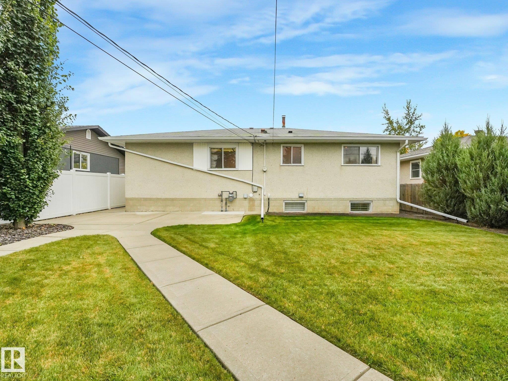 Expansive rear yard featuring a concrete pathway, green lawn, white privacy fence, and mature landscaping - 5904 94 Avenue Nw, Edmonton, AB