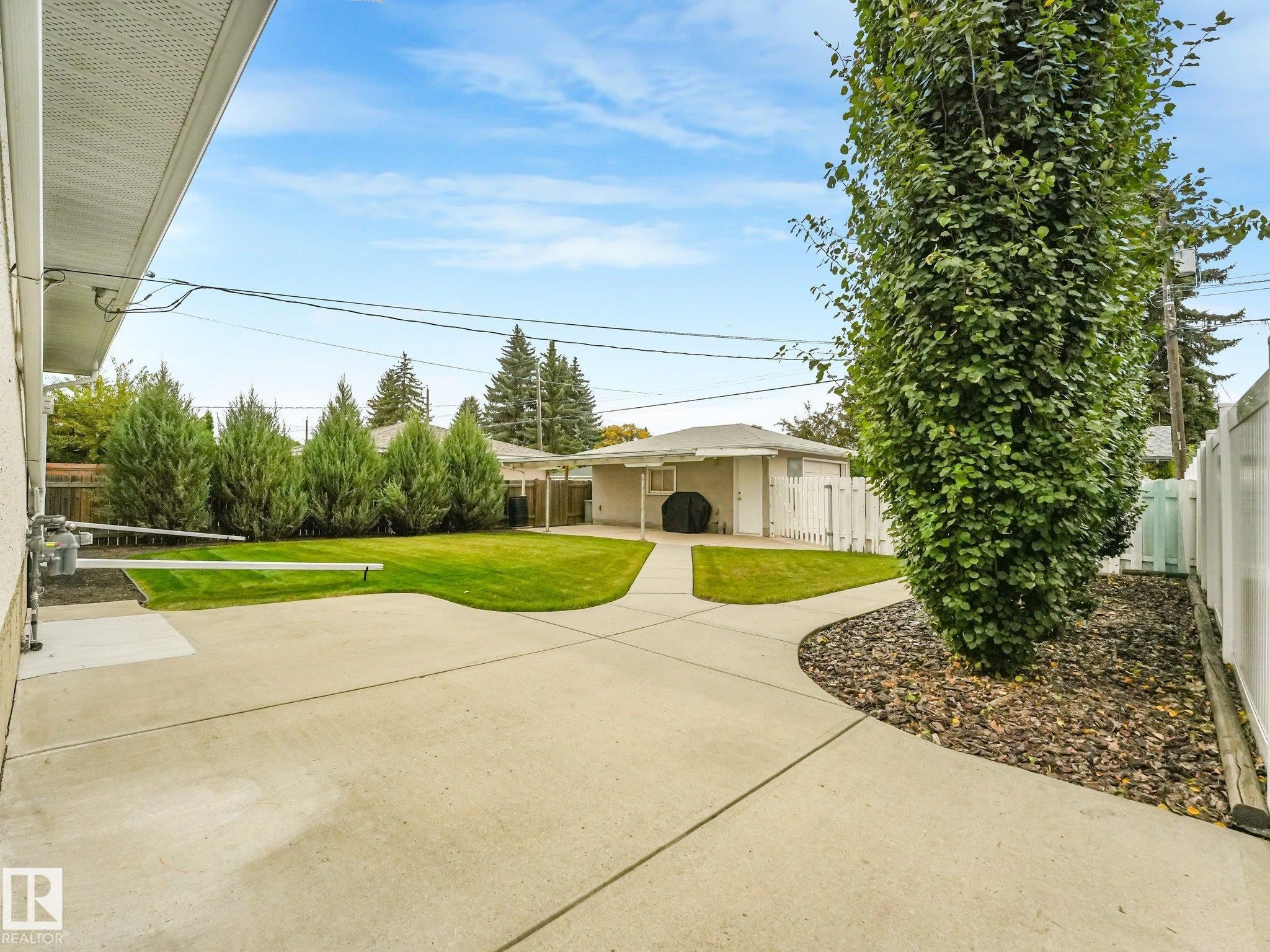 Expansive concrete patio with a manicured lawn, established landscaping, and a privacy fence - 5904 94 Avenue Nw, Edmonton, AB