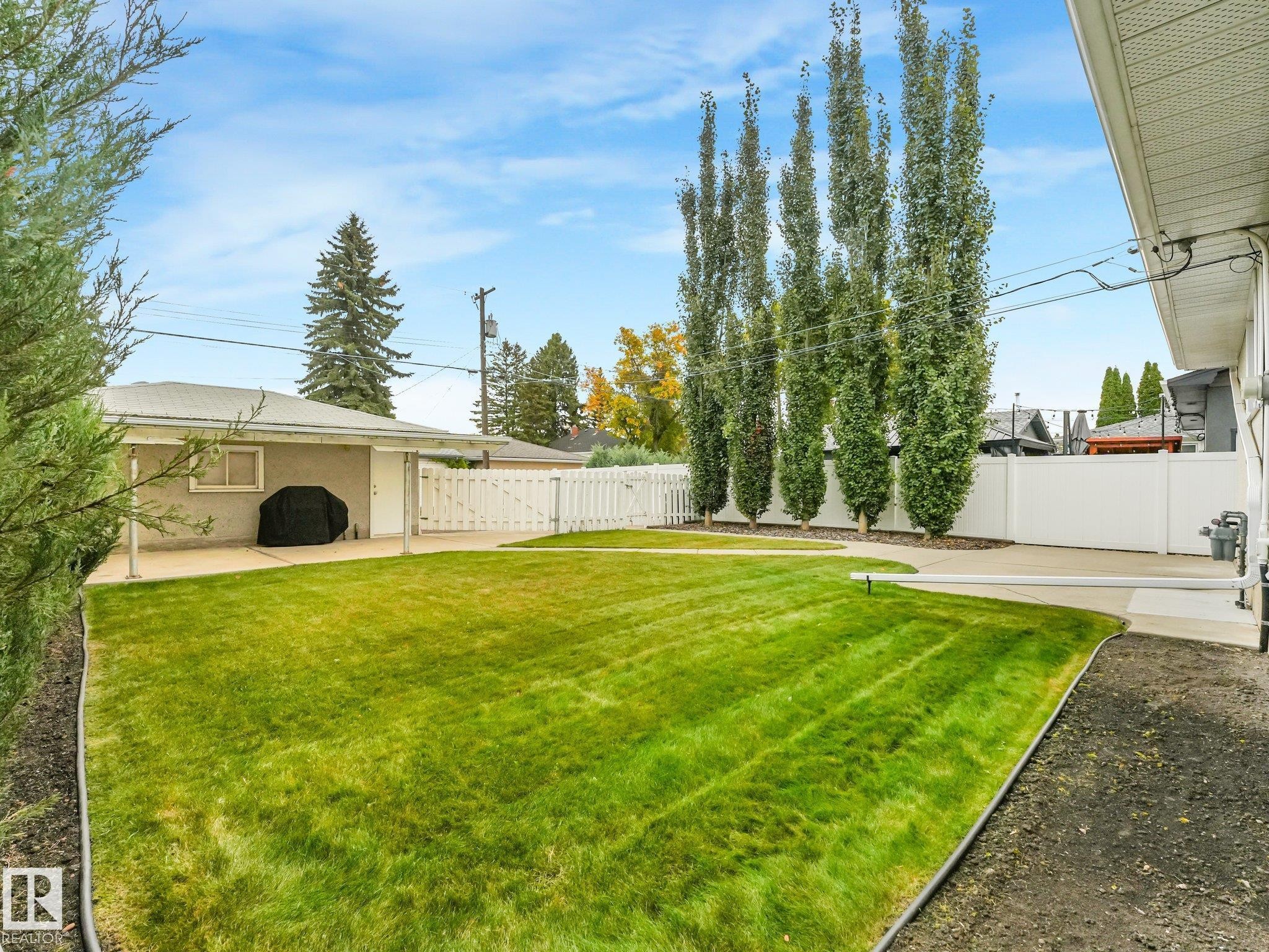 Expansive green lawn, concrete patio, detached garage, white picket fence, and mature trees - 5904 94 Avenue Nw, Edmonton, AB