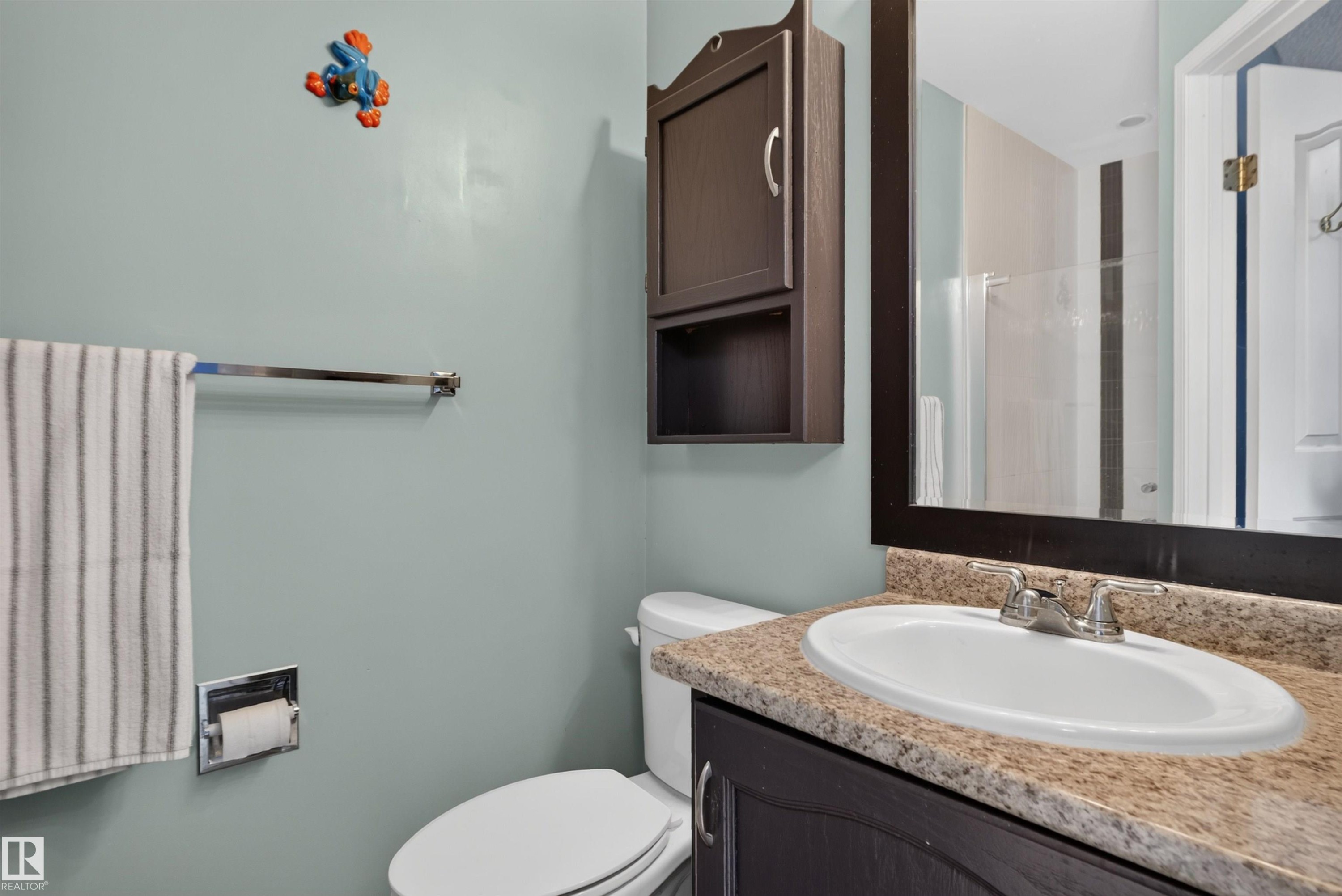 Vanity with an integrated sink and light-toned countertop, framed mirror, and wall-mounted storage cabinet - 1519 104 Street Nw, Edmonton, AB