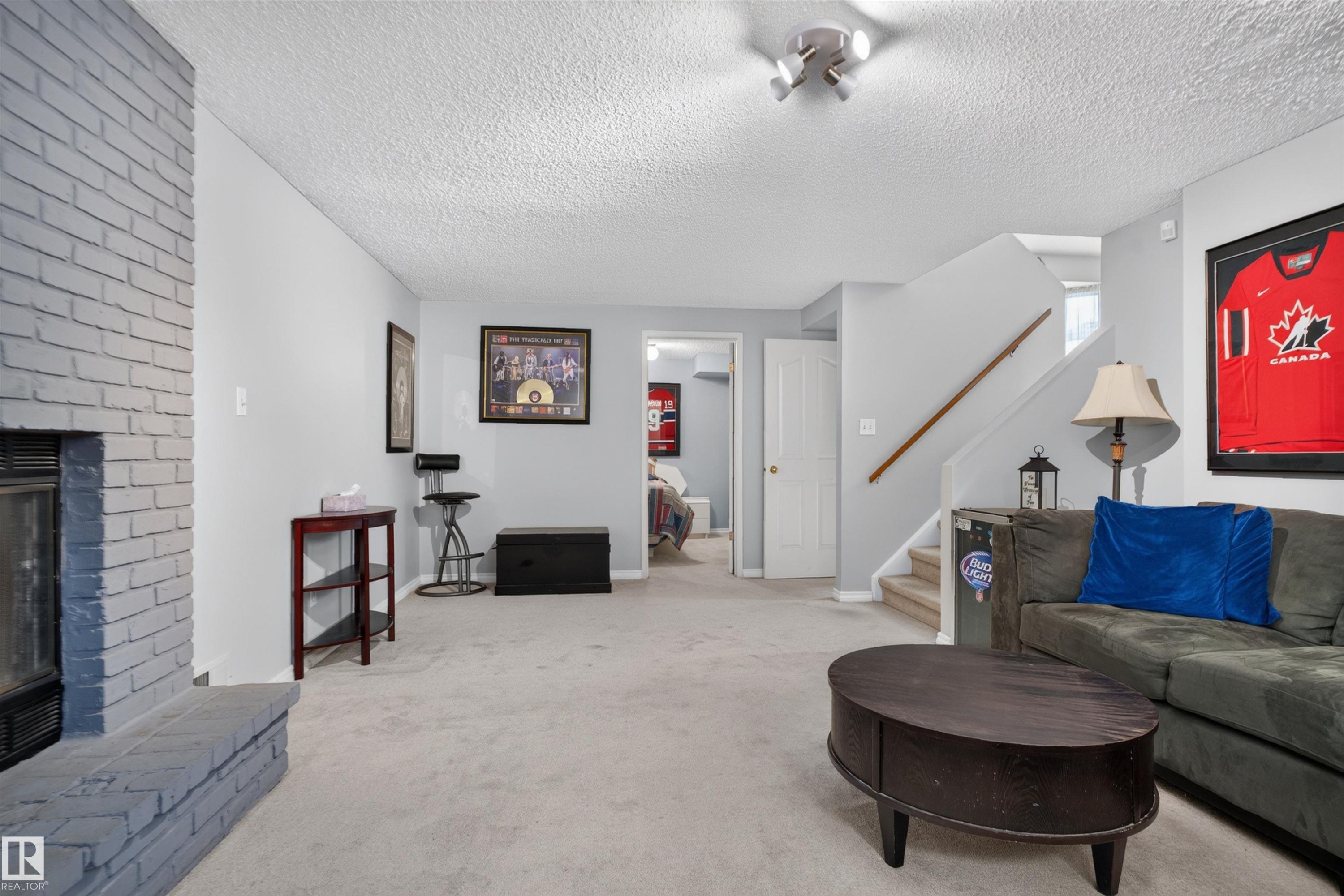 Painted brick fireplace, light-toned carpeting, white interior doors, and a wood handrail on the staircase - 1519 104 Street Nw, Edmonton, AB