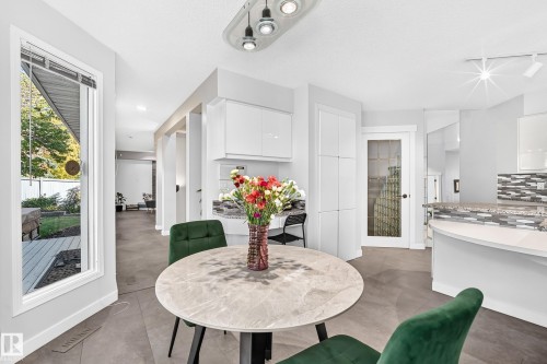 White kitchen cabinetry with integrated appliances, a mosaic tile backsplash, and a curved breakfast bar - 5830 181 Street Nw, Edmonton, AB 