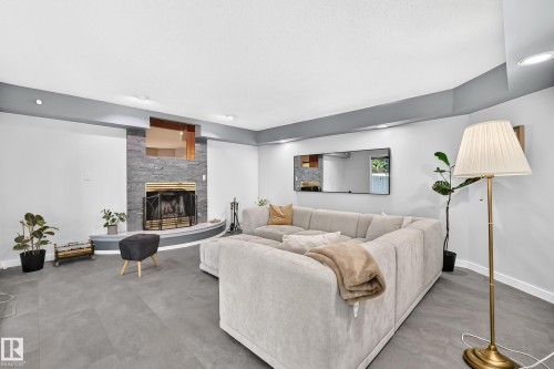 Stone-clad fireplace with a brass fire screen and hearth, gray flooring, recessed lighting, and a soffit ceiling - 5830 181 Street Nw, Edmonton, AB 