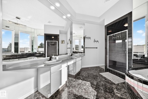 Dual vanities with undermount sinks, expansive mirrored wall, black tile flooring, walk-in shower with frosted glass, and a built-in soaking tub - 5830 181 Street Nw, Edmonton, AB 