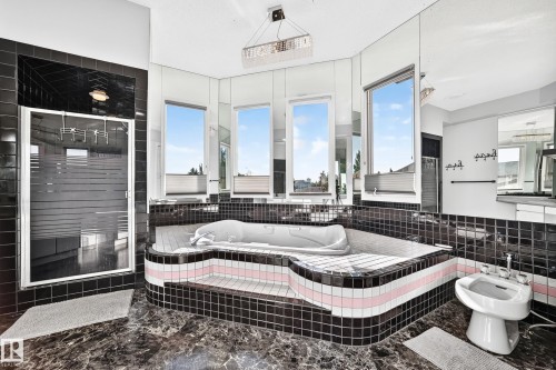Black tiled bathroom featuring a built-in tub with a striped accent, an enclosed shower, a bidet, and multiple windows - 5830 181 Street Nw, Edmonton, AB 