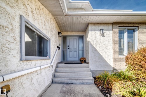 Textured stucco exterior, brick accent wall, concrete entry steps, light gray entry door, and outdoor wall sconces - 5830 181 Street Nw, Edmonton, AB 