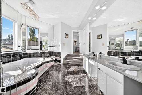 Soaking tub with tiled surround, dual windows, marble-finish flooring, dual vanity with undermount sinks, and built-in mirrored wall - 5830 181 Street Nw, Edmonton, AB 