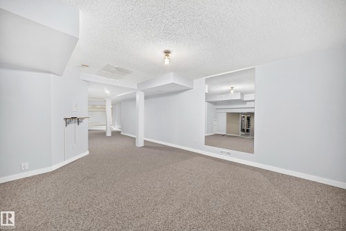 Open-concept room featuring neutral carpeting, light-toned wall paint, and exposed structural columns - 5830 181 Street Nw, Edmonton, AB 
