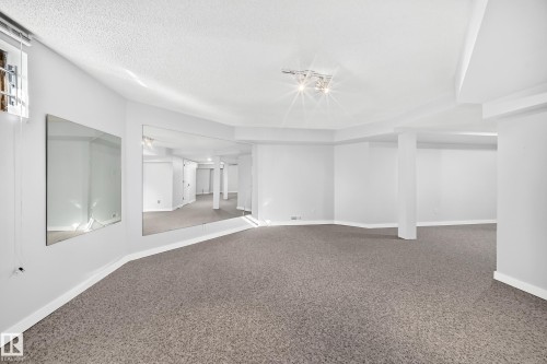 Expansive room with carpet flooring, track lighting, and a large wall-mounted mirror - 5830 181 Street Nw, Edmonton, AB 