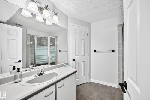 Vanity with integrated sink, three-light fixture, mirror, and white paneled cabinetry - 5830 181 Street Nw, Edmonton, AB 