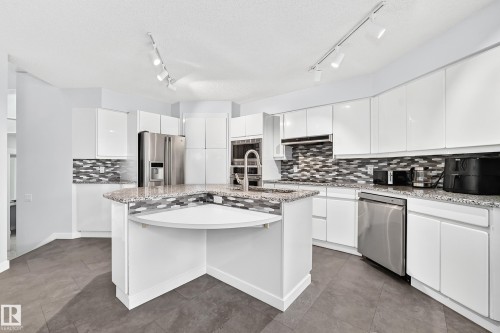Kitchen featuring white cabinetry, granite countertops, stainless steel appliances, a mosaic tile backsplash, and track lighting - 5830 181 Street Nw, Edmonton, AB 